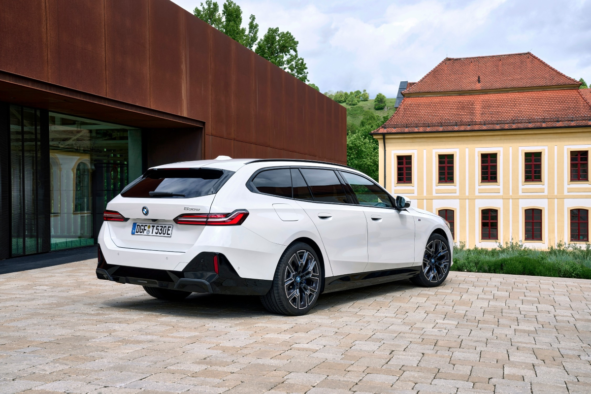 bmw-g61-easyimport-04_1 Parte trasera 3/4 BMW 530e Touring G61 Blanco aparcado delante de un edificio marrón.