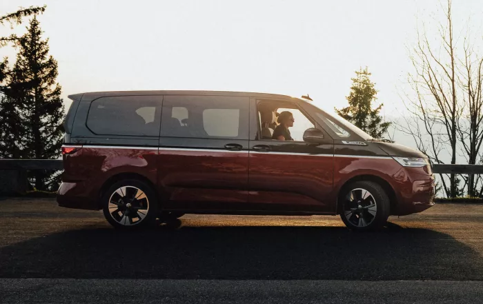 Vista lateral de Volkswagen T7 Multivan bicolor rojo-negro. Vista de lateral frente al atardecer